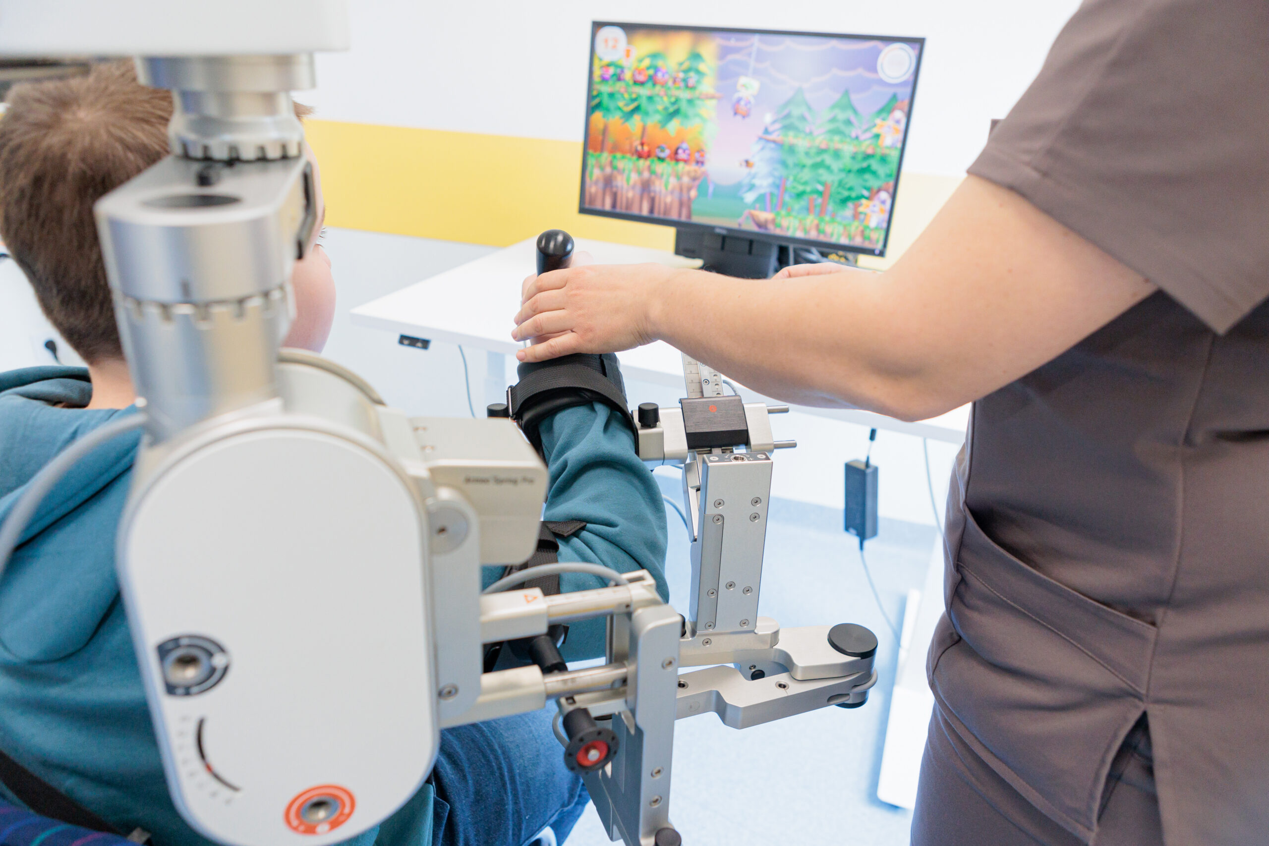 Child receiving robotic arm therapy while interacting with a game on screen in a pediatric rehab clinic. High quality photo
