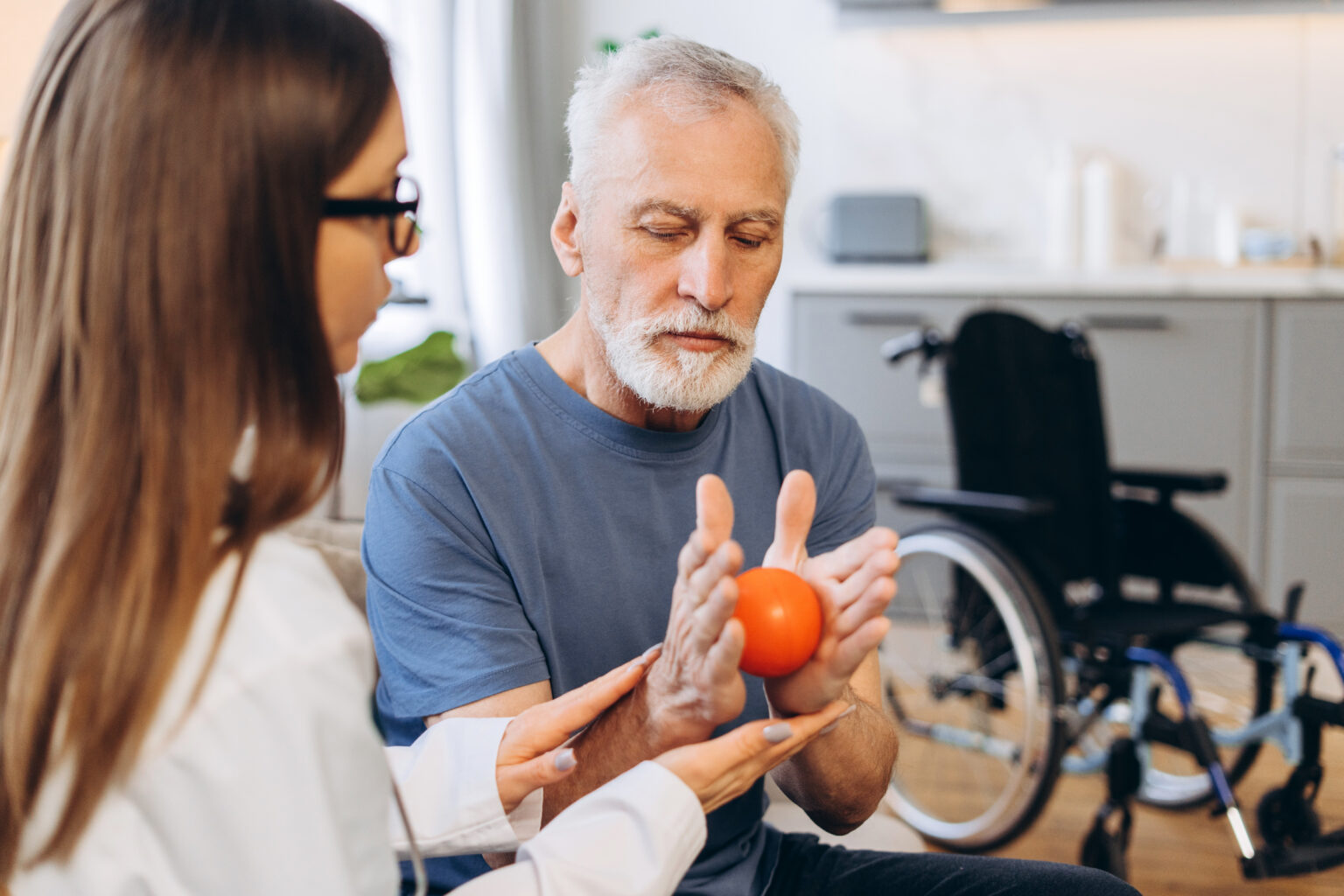 Healthcare worker assisting senior man with hand therapy using a stress ball during a home rehabilitation session