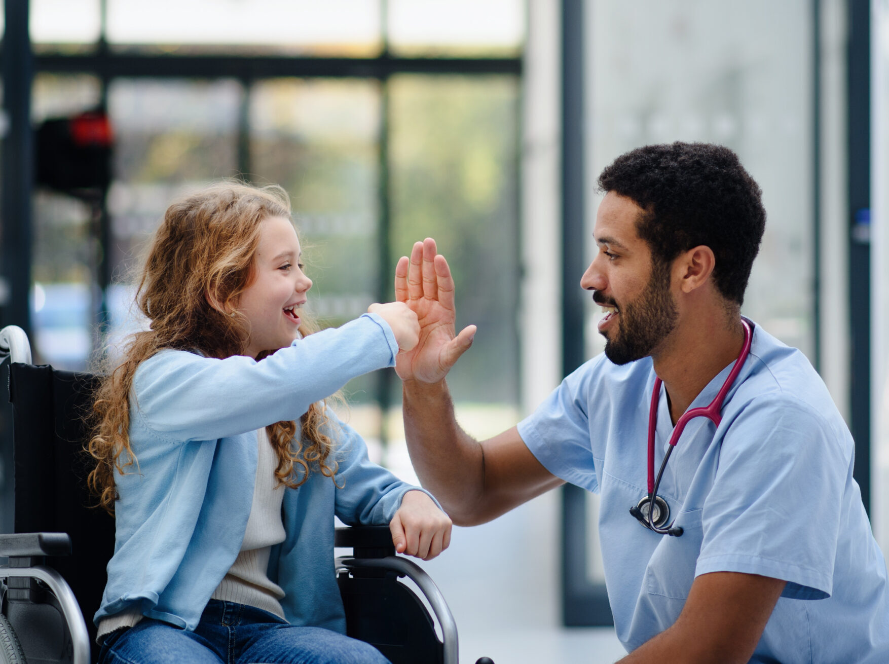 Young multiracial doctor having fun with little girl on a wheelchair.